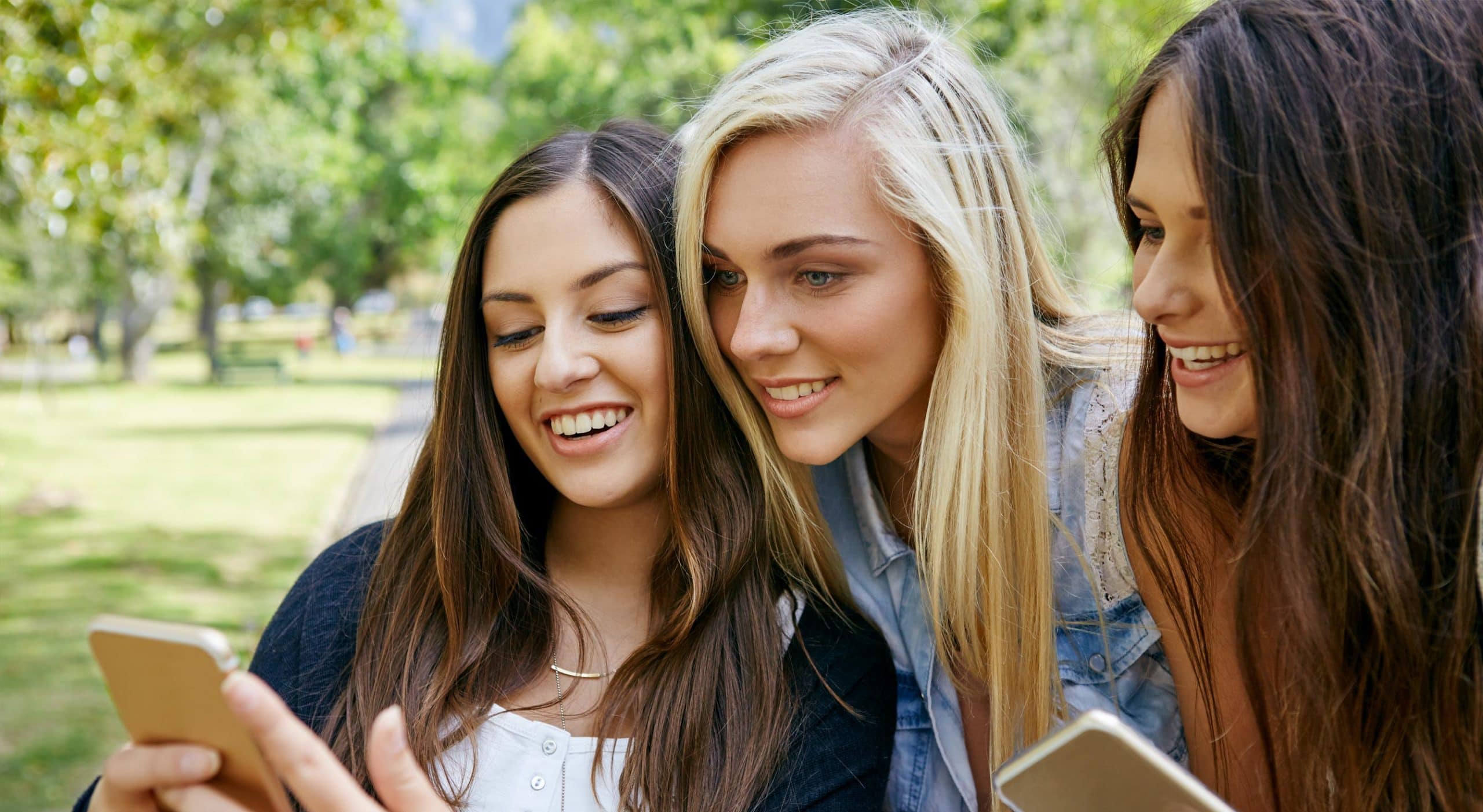 Three young women with cell phones in their hands looking for jobs at Frutura